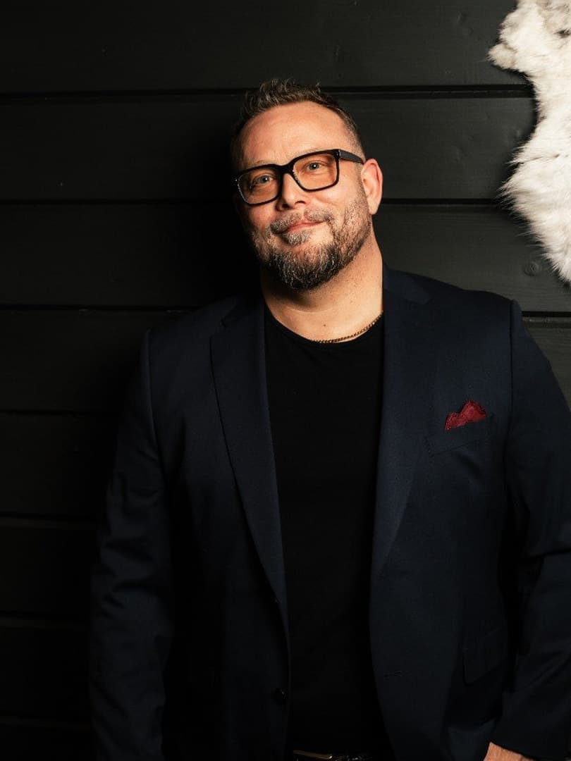 Petri Juotasniemi in a dark blazer against a black timber wall